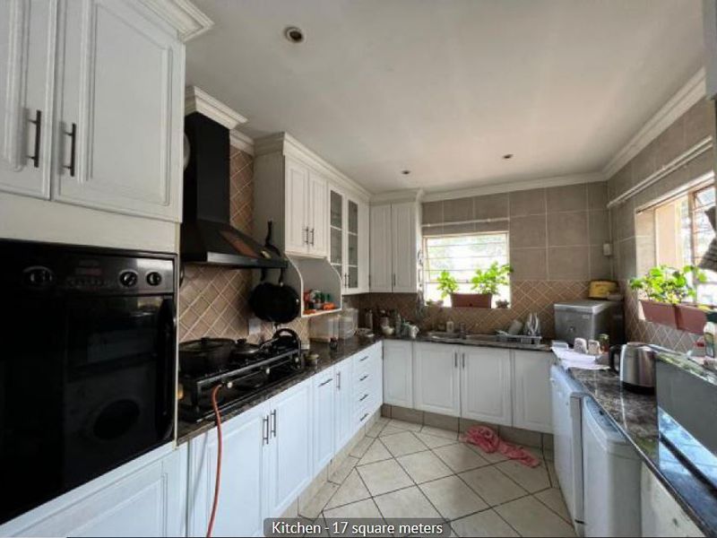 A functional kitchen featuring white cabinetry, granite countertops, a built-in oven, gas hob, and tiled finishes throughout.