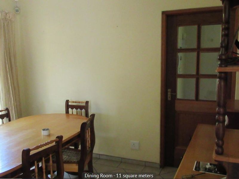 A functional dining room featuring tiled flooring, a timber-framed glass door, and a window with security bars.