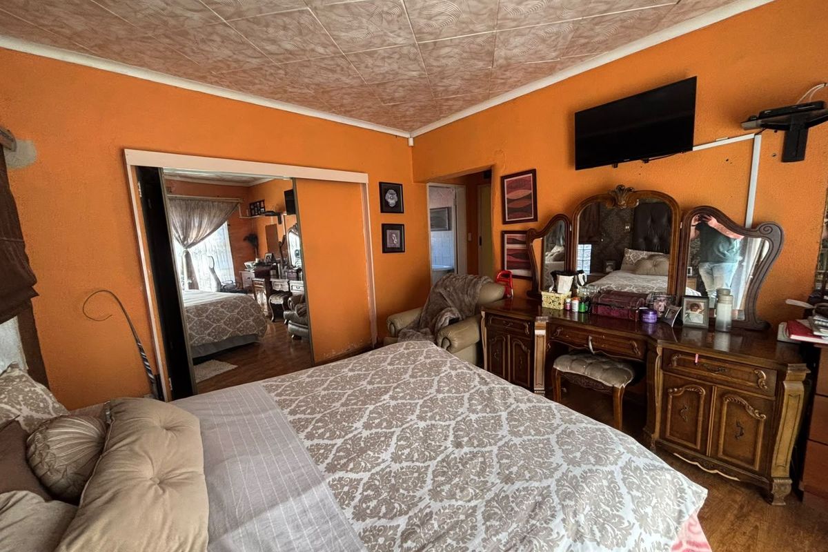 A bedroom featuring laminate flooring, textured ceiling tiles, and mirrored sliding wardrobe doors, currently finished with vibrant orange wall paint.