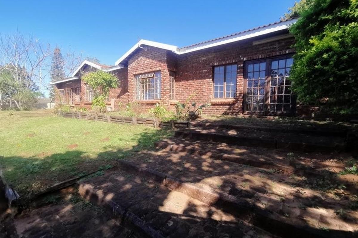 Rear view of a single-story exposed brick house featuring timber-framed windows and doors, leading out to a garden area with brick steps.
