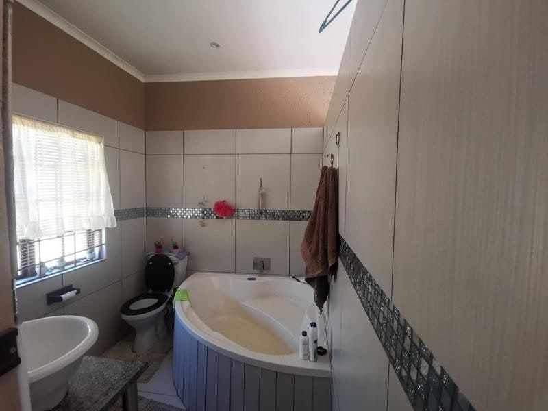 A functional bathroom featuring a corner bathtub, pedestal basin, and toilet, finished with neutral wall tiles and a decorative mosaic border.