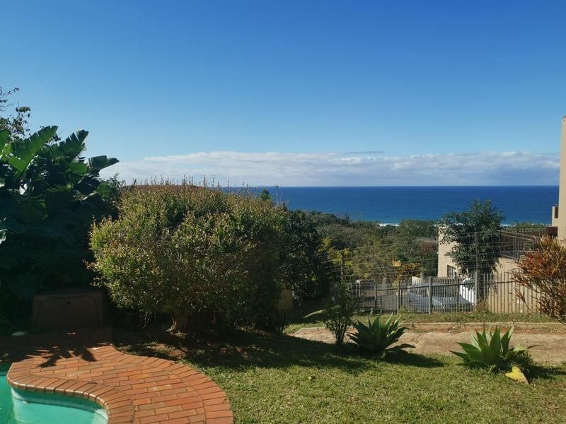 A scenic outdoor view featuring a swimming pool with brick coping, overlooking a lush garden and the distant ocean horizon.