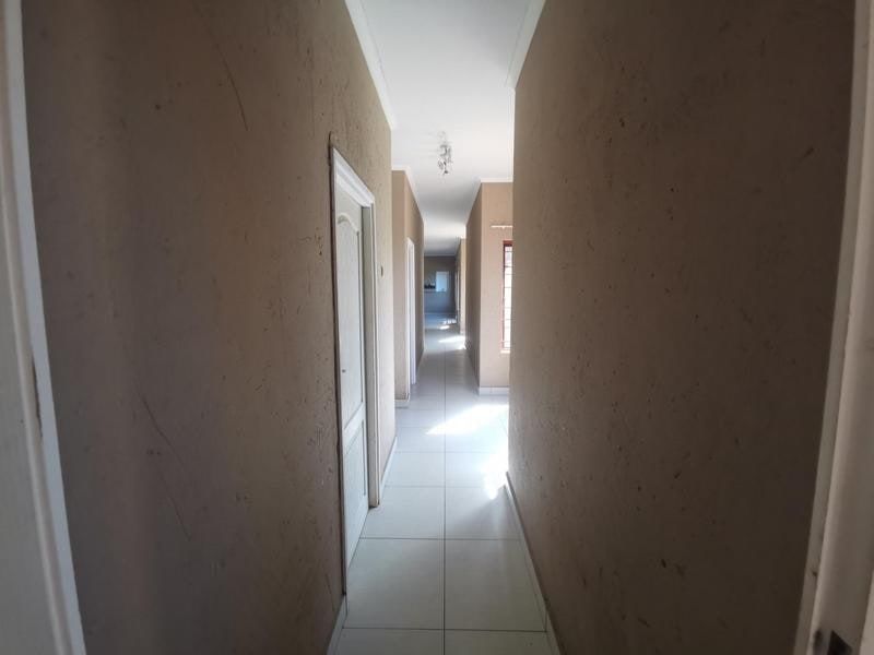 A long, empty hallway featuring tiled flooring and multiple internal doors, requiring cosmetic attention to the wall finishes.