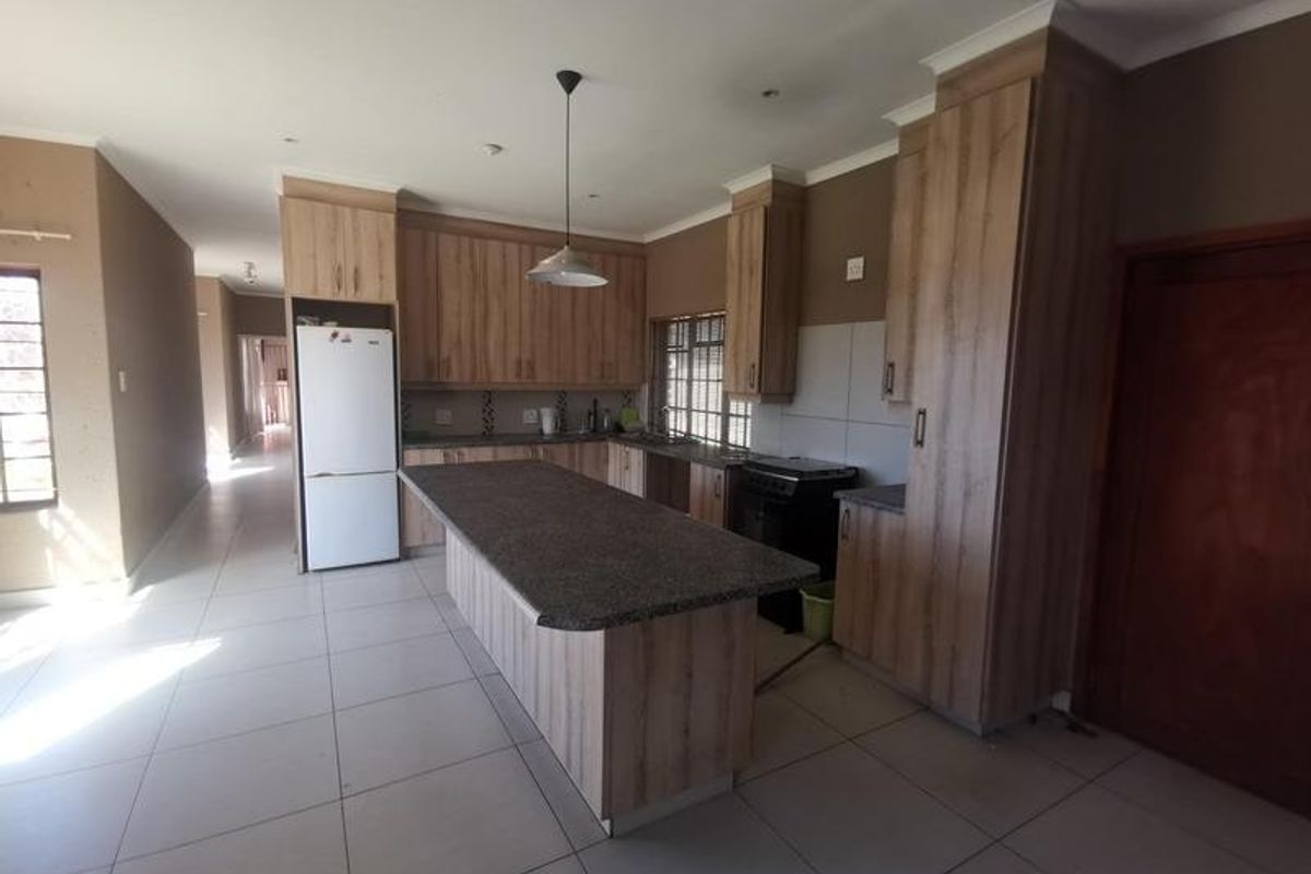 A spacious kitchen featuring modern wood-finish cabinetry, a large central island with stone countertops, tiled flooring, and integrated lighting.