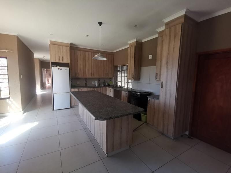 A spacious kitchen featuring modern wood-finish cabinetry, a large central island with stone countertops, tiled flooring, and integrated lighting.
