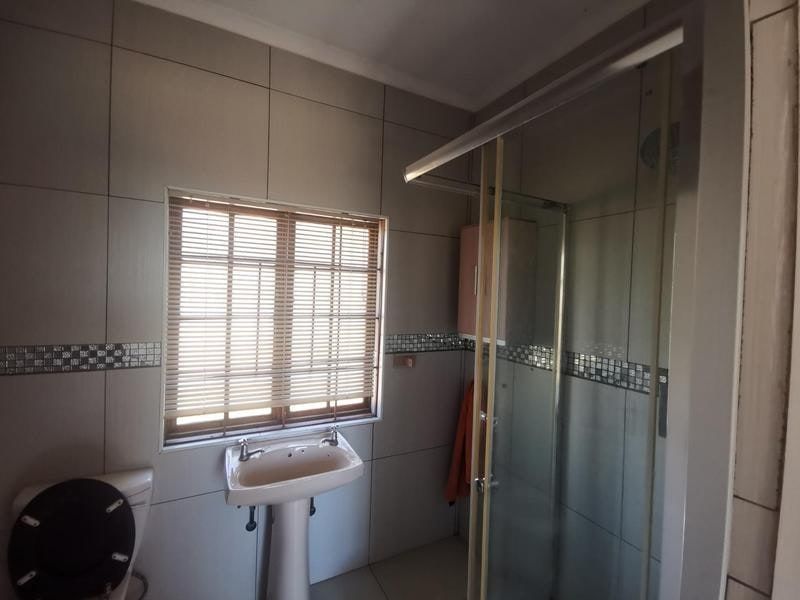 A functional bathroom featuring a pedestal basin, a glass-enclosed shower, and neutral wall tiling with a decorative mosaic border.