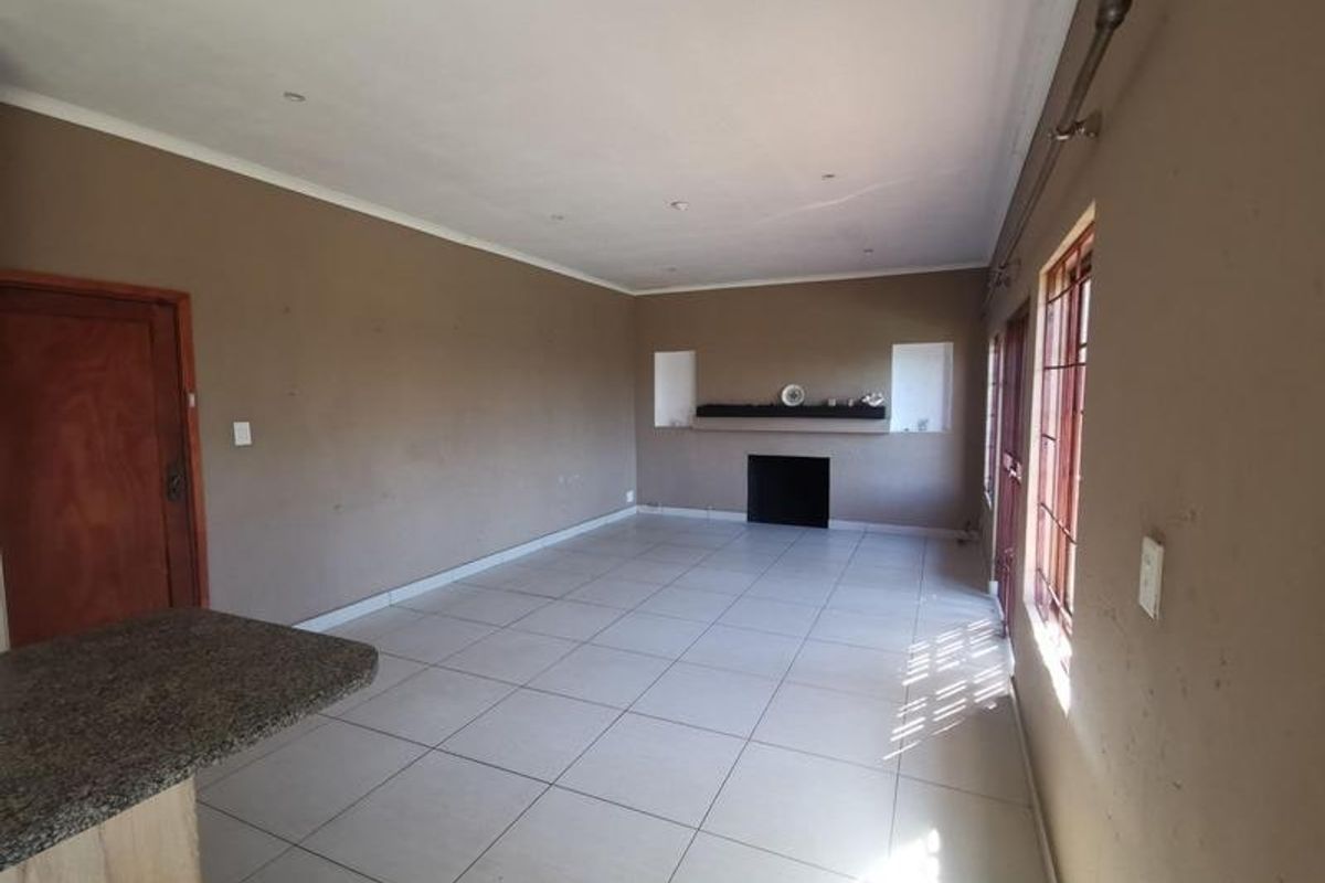 An empty living room featuring tiled flooring, a built-in fireplace with recessed shelving, and a granite countertop breakfast bar.