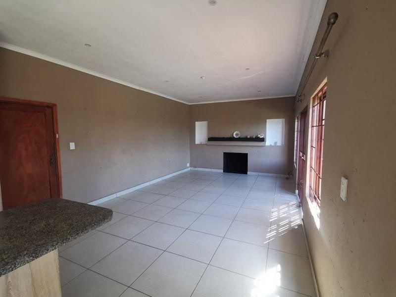 An empty living room featuring tiled flooring, a built-in fireplace with recessed shelving, and a granite countertop breakfast bar.