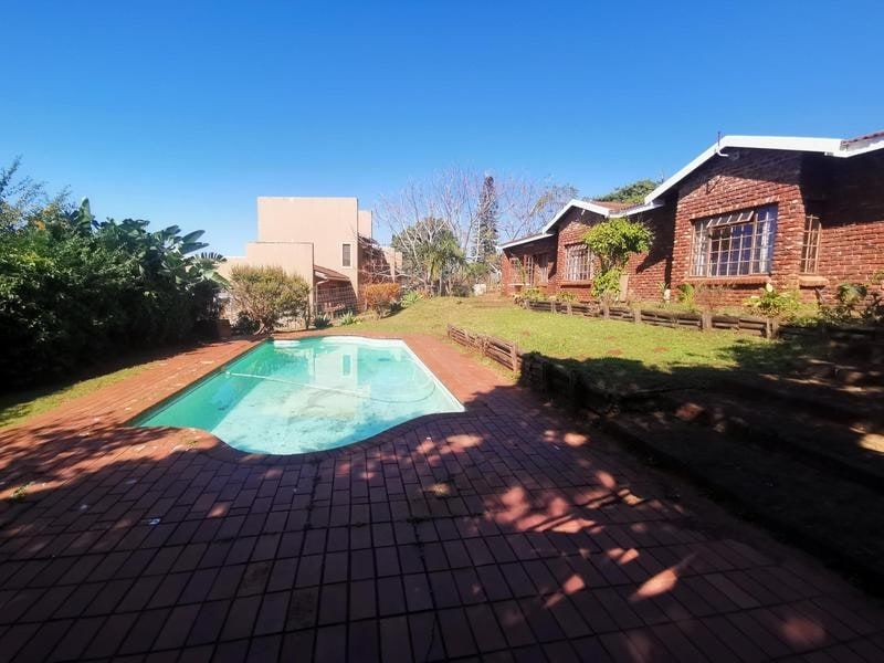 Rear garden area featuring a swimming pool with brick paving and a brick house facade.