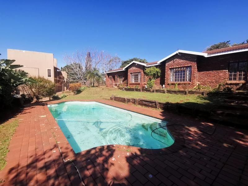 Rear exterior view featuring a swimming pool, brick paved surround, and a face brick house facade with a landscaped garden area.