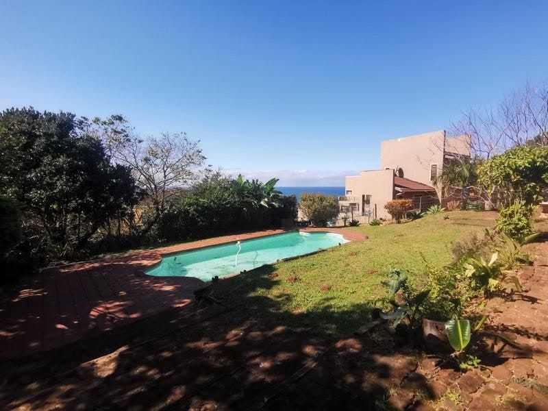 Outdoor pool area featuring a swimming pool, paved patio, and garden with distant ocean views.