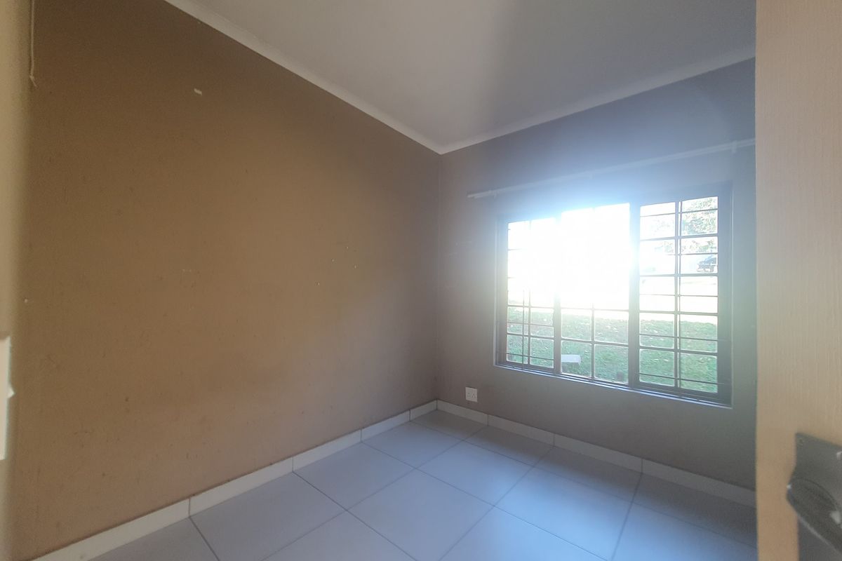 An empty bedroom featuring tiled flooring, neutral wall paint, and a window fitted with security bars.