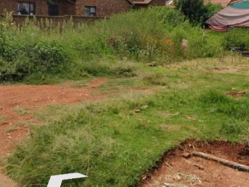 A view of an undeveloped residential plot featuring overgrown grass and natural terrain, suitable for future landscaping or construction projects.