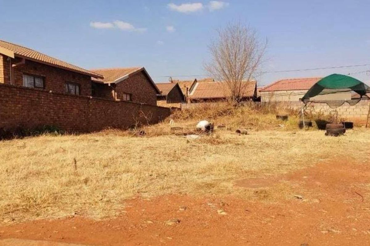 A vacant residential plot featuring perimeter brick walling and natural ground cover, situated within an established neighborhood.