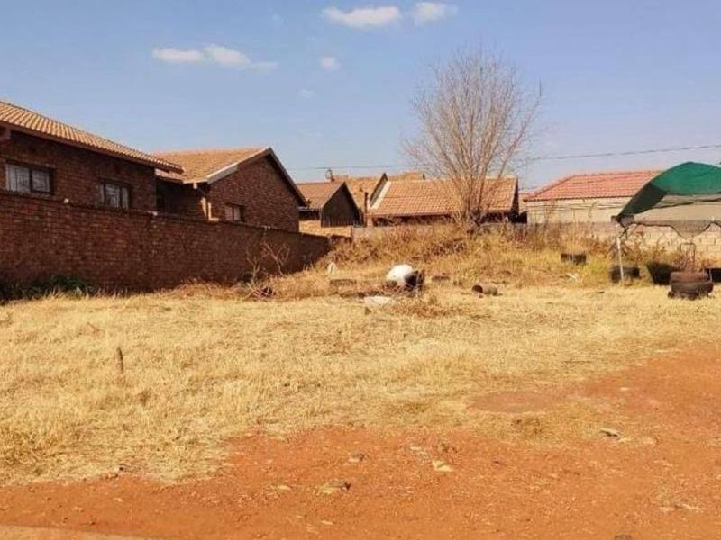 A vacant residential plot featuring perimeter brick walling and natural ground cover, situated within an established neighborhood.