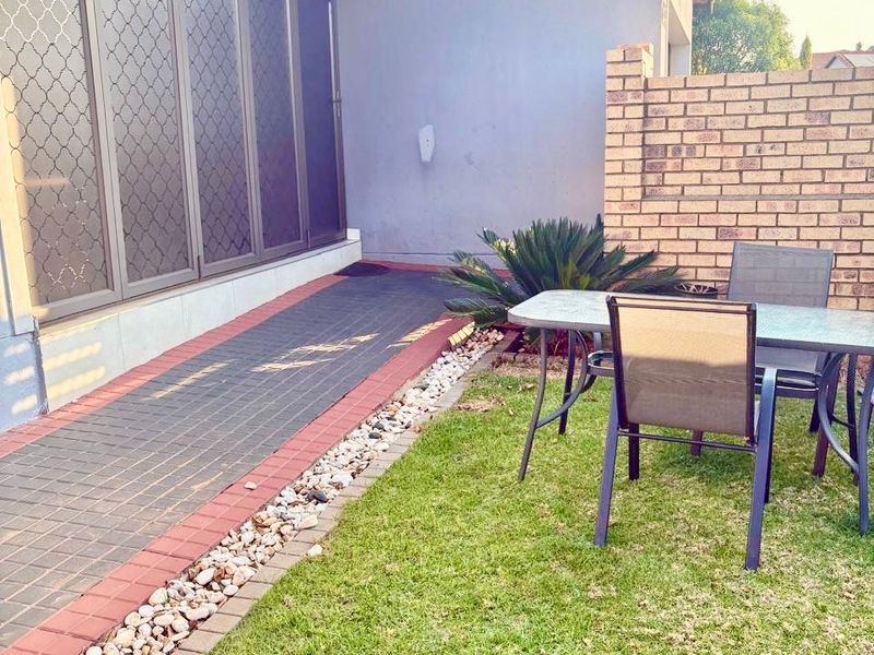 A well-maintained rear garden area featuring a paved walkway, brick boundary wall, and solar panels installed on the tiled roof.