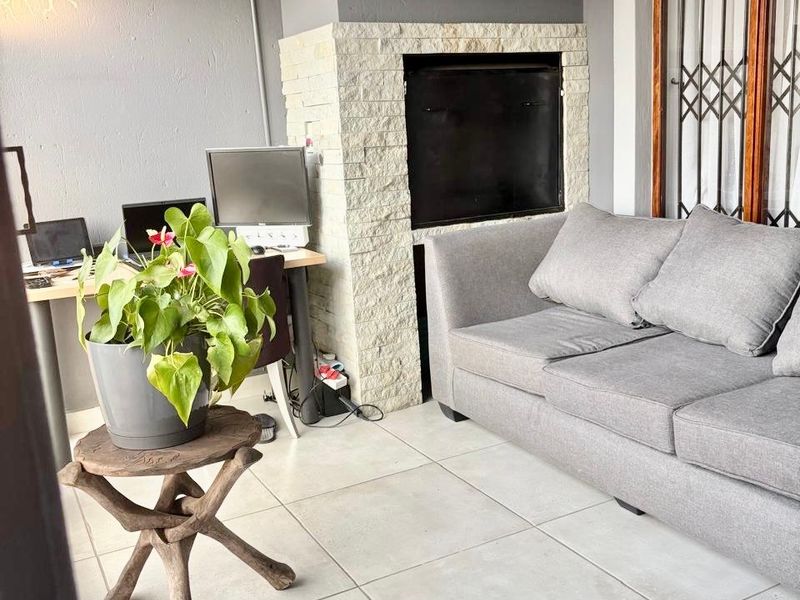 Covered patio area featuring a built-in fireplace with stone cladding, neutral floor tiles, and a secure entrance door.