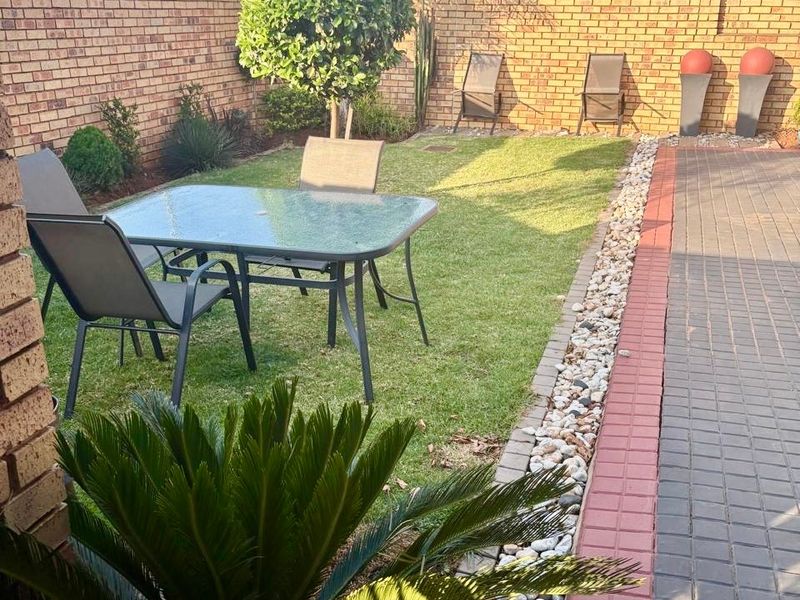 A well-maintained rear garden featuring a neat lawn, paved walkway, and brick boundary walls, providing a private outdoor space.