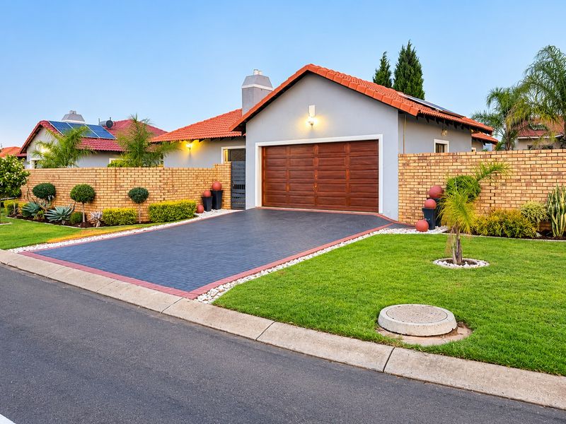 Well-maintained front exterior featuring a paved driveway, brick boundary wall, tiled roof, and a modern sectional garage door.