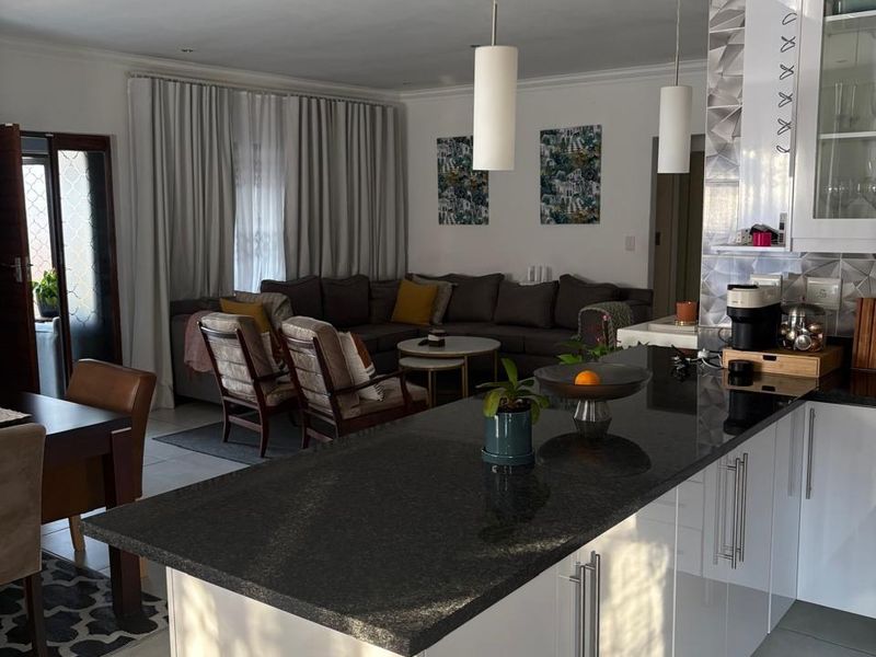 Spacious open-plan living area featuring a modern kitchen with a granite-topped island, sleek cabinetry, and integrated lighting, flowing into a comfortable lounge space.
