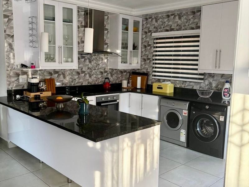 Modern kitchen featuring white cabinetry, granite countertops, geometric tiled backsplash, and integrated laundry appliances with a functional island layout.