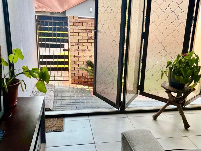 A covered patio area featuring modern folding glass doors that open onto a paved outdoor space with a brick boundary wall.