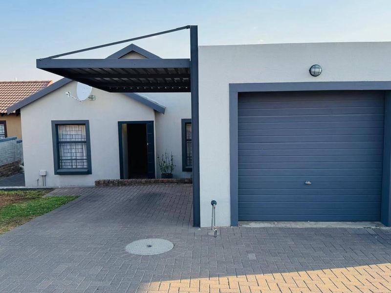 Front elevation of a townhouse featuring a paved driveway, single garage, and a covered carport area.
