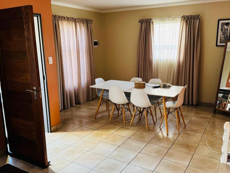 A functional dining room featuring tiled flooring, a solid wooden door, and windows fitted with security bars, offering a neutral and practical living space.