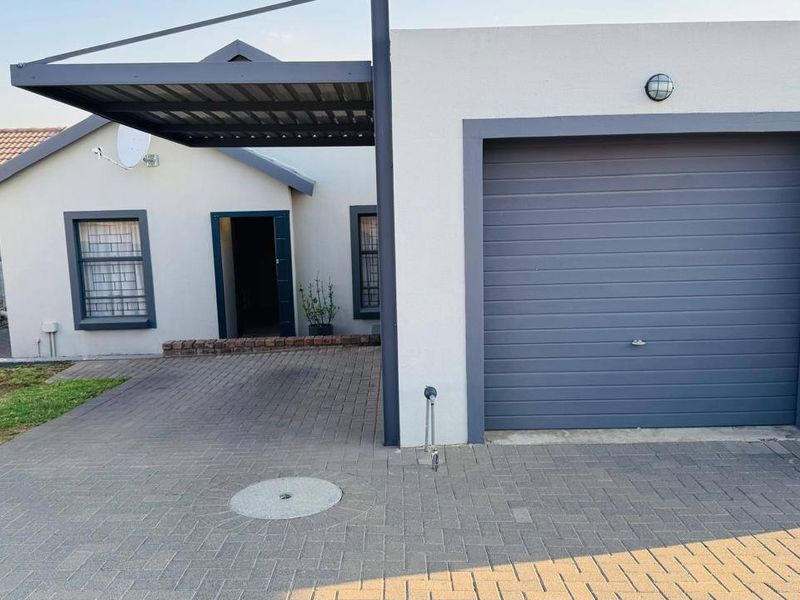 Front view of a townhouse featuring a paved driveway, single garage, and a covered carport area.