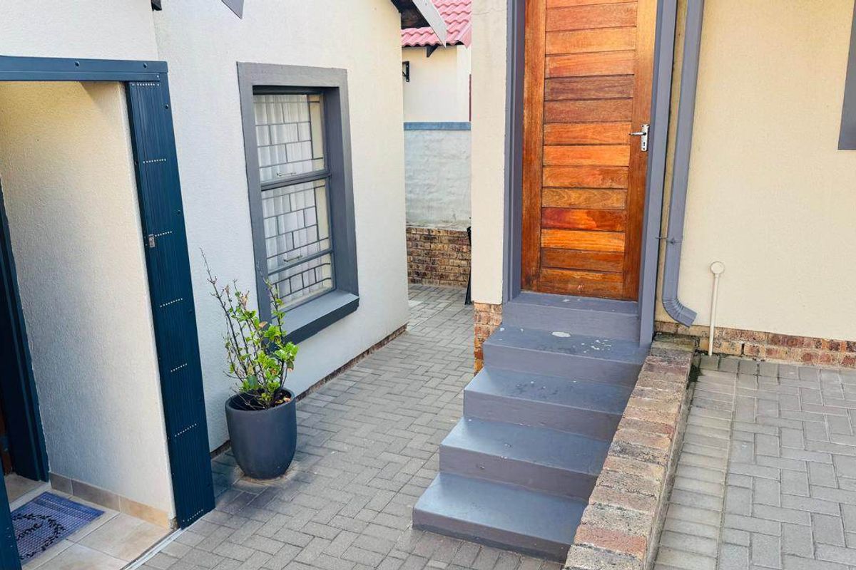 A paved rear courtyard area featuring a timber entrance door, concrete steps, and a brick retaining wall.