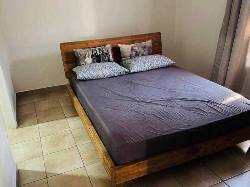 A functional bedroom featuring neutral tiled flooring and window treatments, providing a clean and simple space.