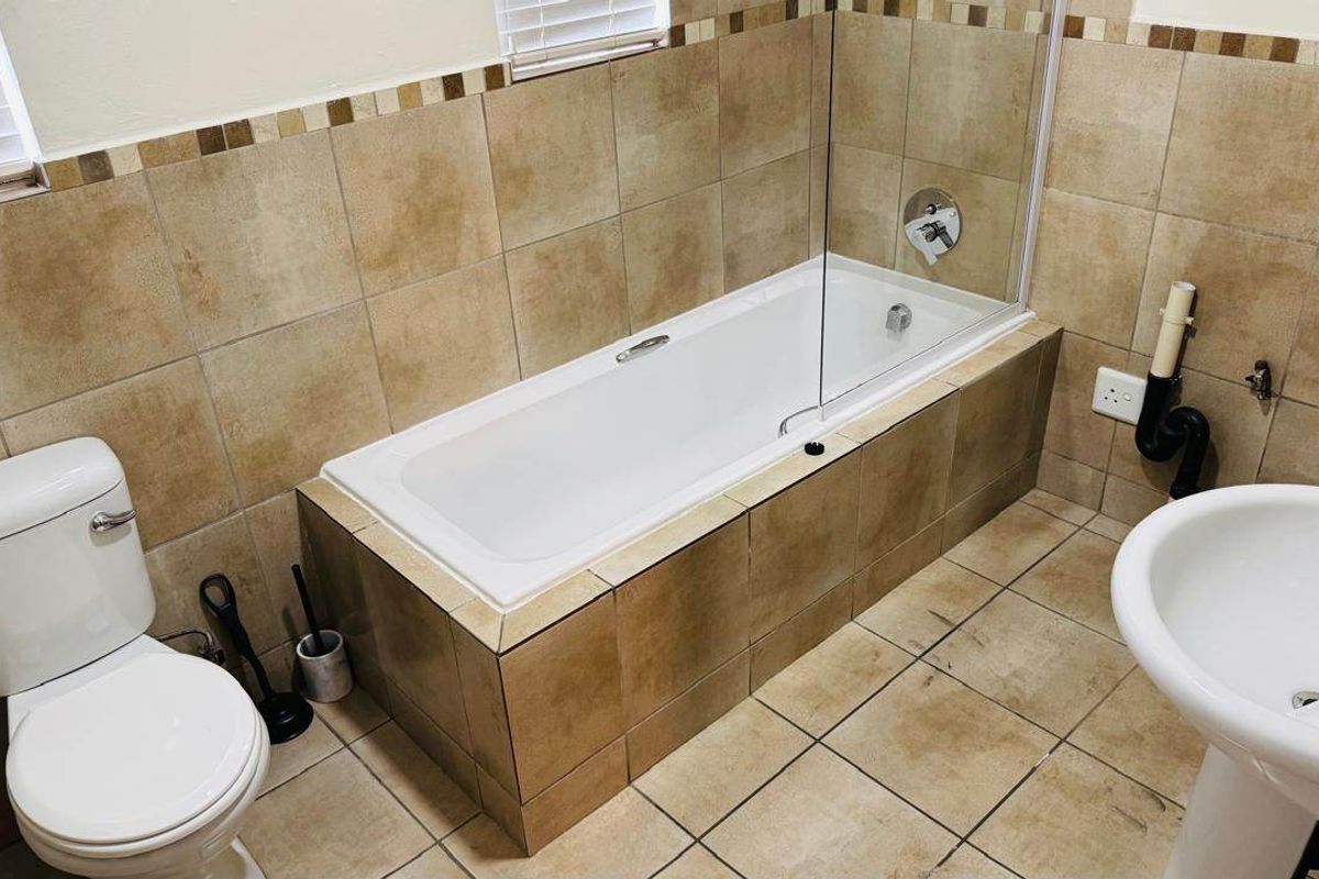 A functional bathroom featuring a bathtub with a glass screen, pedestal sink, and toilet, finished with neutral ceramic tiling throughout.