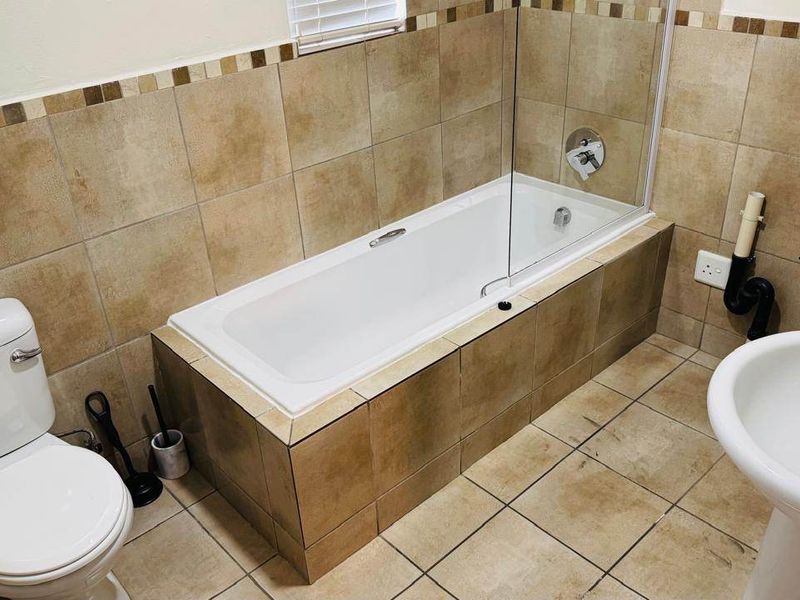 A functional bathroom featuring a bathtub with a glass screen, pedestal sink, and toilet, finished with neutral ceramic tiling throughout.