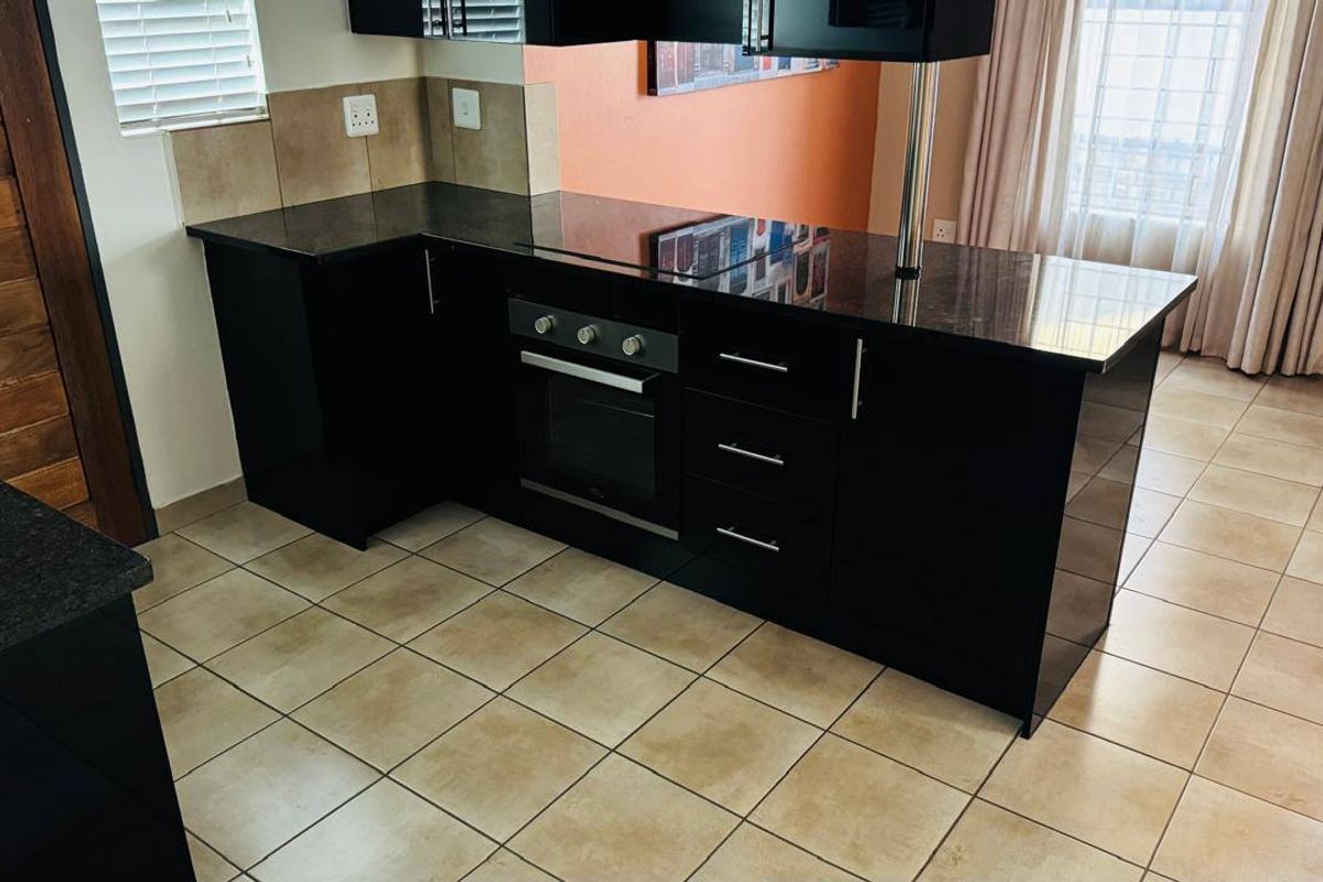 Modern kitchen featuring sleek black cabinetry, granite countertops, a built-in oven, and a functional breakfast bar layout with ceramic tiled flooring.