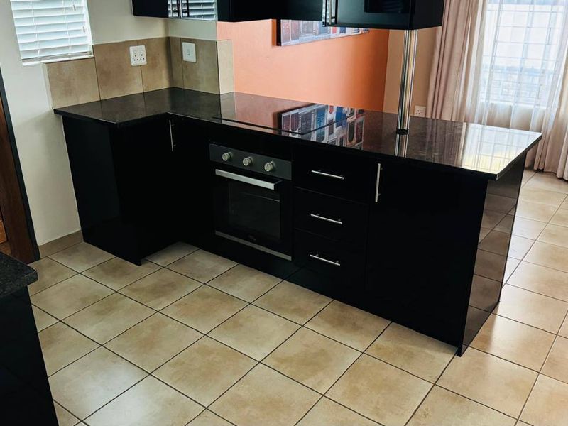 Modern kitchen featuring sleek black cabinetry, granite countertops, a built-in oven, and a functional breakfast bar layout with ceramic tiled flooring.