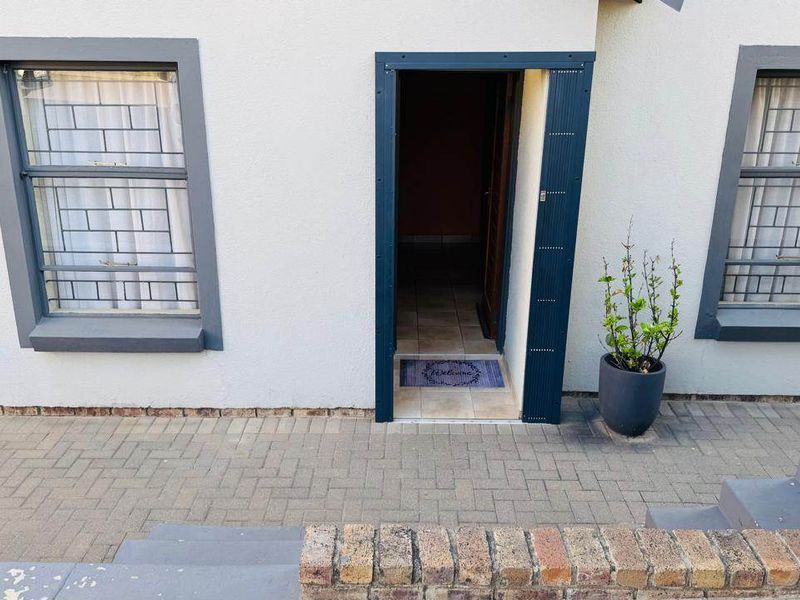 Front entrance of the townhouse featuring paved access, security-barred windows, and a brick retaining wall.