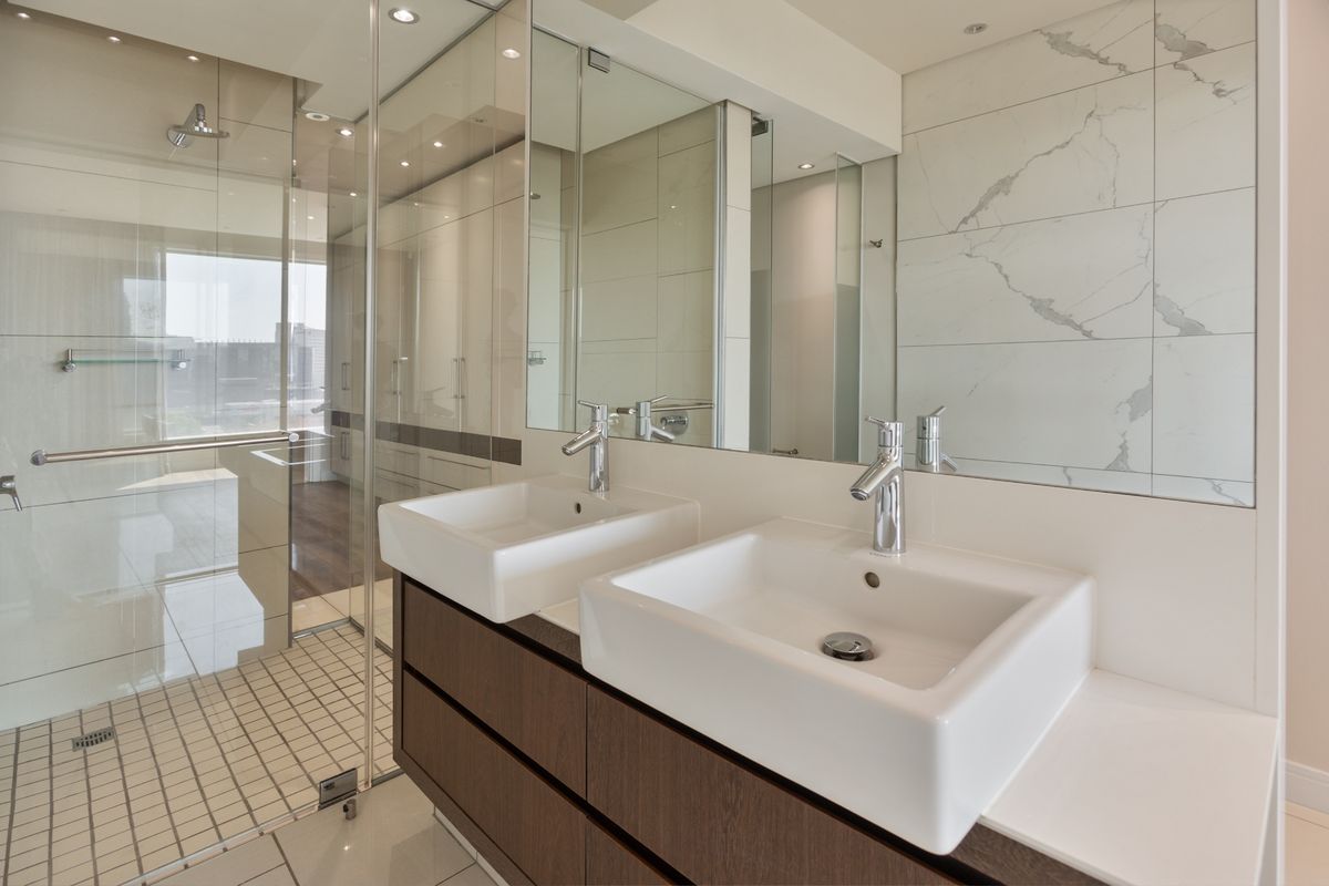 Modern bathroom featuring a double vanity with vessel sinks, chrome fixtures, and a spacious walk-in shower with glass enclosure and marble-look wall tiles.