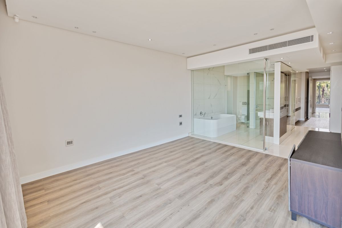 Spacious bedroom featuring modern laminate flooring, recessed lighting, and a sleek glass-enclosed ensuite bathroom with a freestanding bathtub.