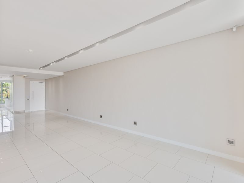 A bright, spacious, and empty living area featuring polished porcelain tile flooring, recessed ceiling lighting, and neutral wall finishes.