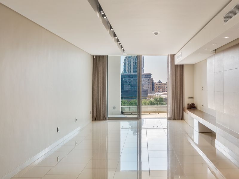 A bright, modern, and empty living area featuring polished tiled floors, recessed lighting, ducted air conditioning, and a built-in media console with balcony access.