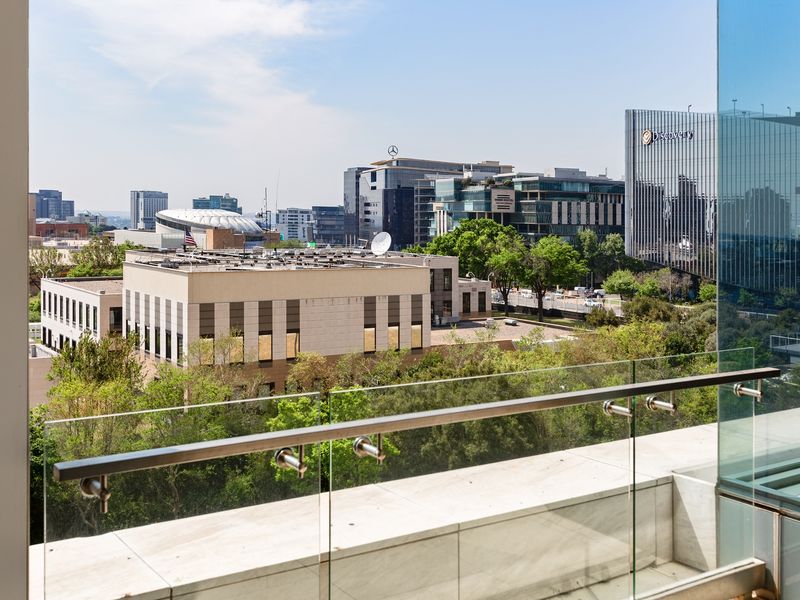 A clear view of the surrounding urban landscape from a modern apartment balcony featuring a sleek glass balustrade and stone flooring.