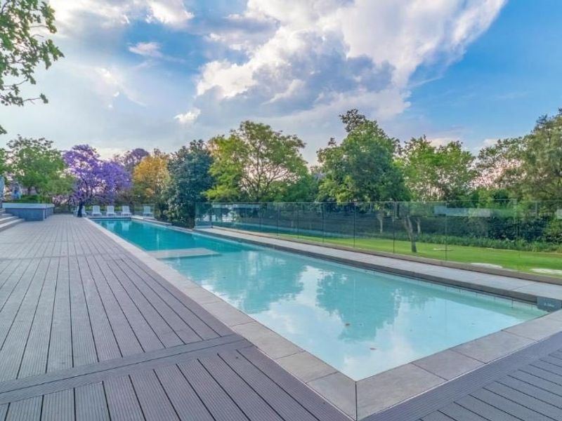 A well-maintained outdoor swimming pool area featuring modern composite decking and a sleek glass balustrade overlooking a landscaped garden.