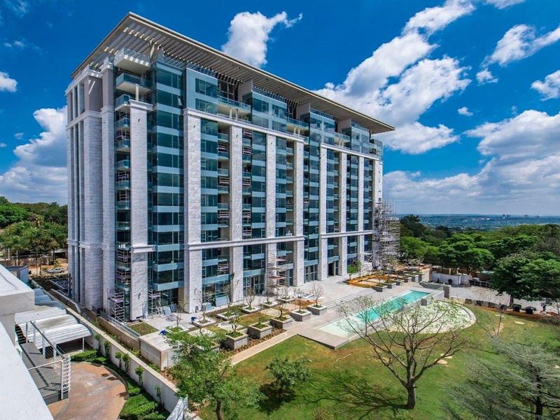 Aerial view of a modern high-rise apartment building featuring glass balconies, a swimming pool, and landscaped grounds.