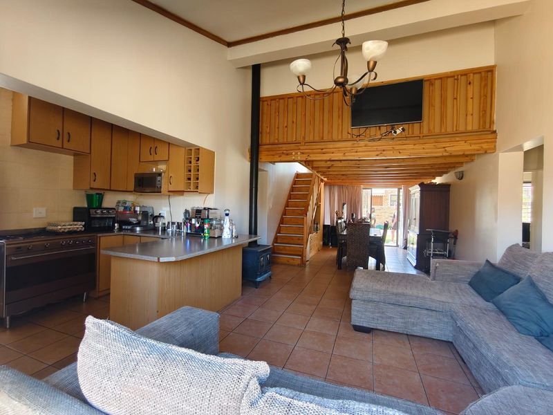 Open-plan living area featuring a kitchen with wooden cabinetry, a central island, a wood-burning fireplace, and a mezzanine level with a wooden staircase.