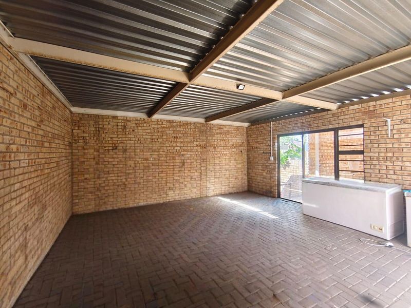 A covered outdoor patio area featuring exposed brick walls, paved flooring, and a corrugated metal roof, providing a versatile space for outdoor living.