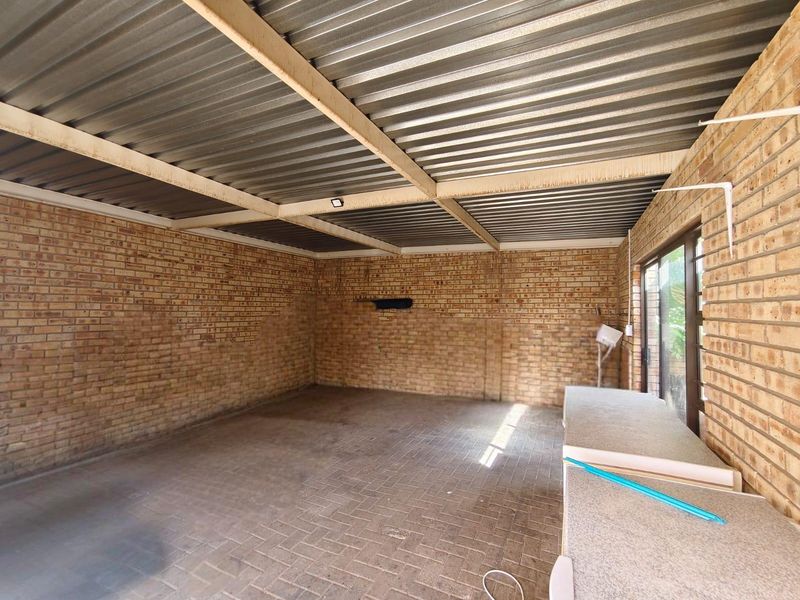 A covered outdoor patio area featuring exposed brick walls, a corrugated metal roof, and paved flooring, providing a versatile space for outdoor living.