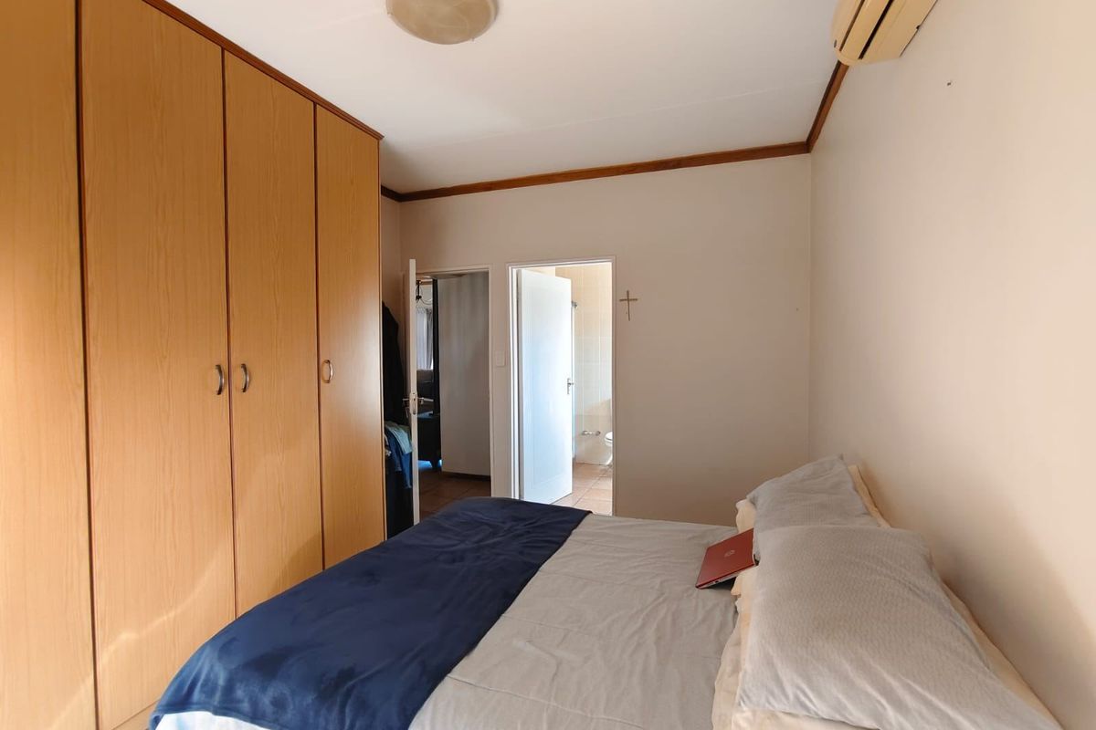 A functional bedroom featuring built-in wooden cupboards, a wall-mounted air conditioning unit, and direct access to an adjoining bathroom.