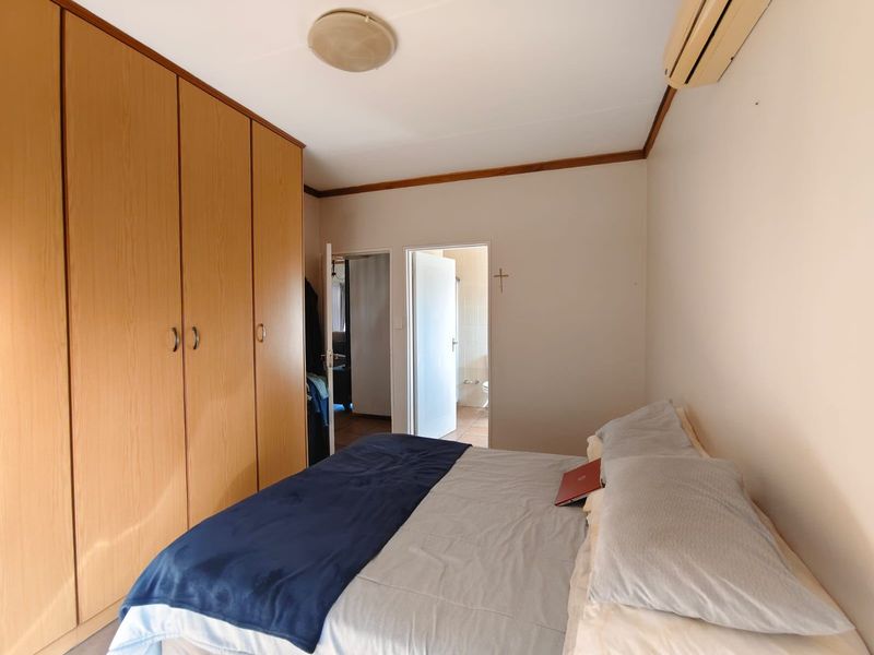 A functional bedroom featuring built-in wooden cupboards, a wall-mounted air conditioning unit, and direct access to an adjoining bathroom.