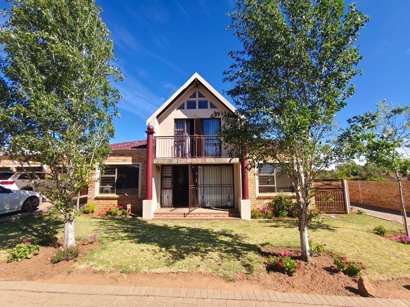 Front elevation of a two-story townhouse featuring a brick facade, a balcony with metal railings, and a paved driveway.