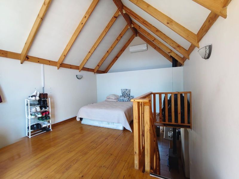 A loft-style bedroom featuring exposed timber rafters, polished timber flooring, and a split-system air conditioner, overlooking the lower level via a timber staircase.